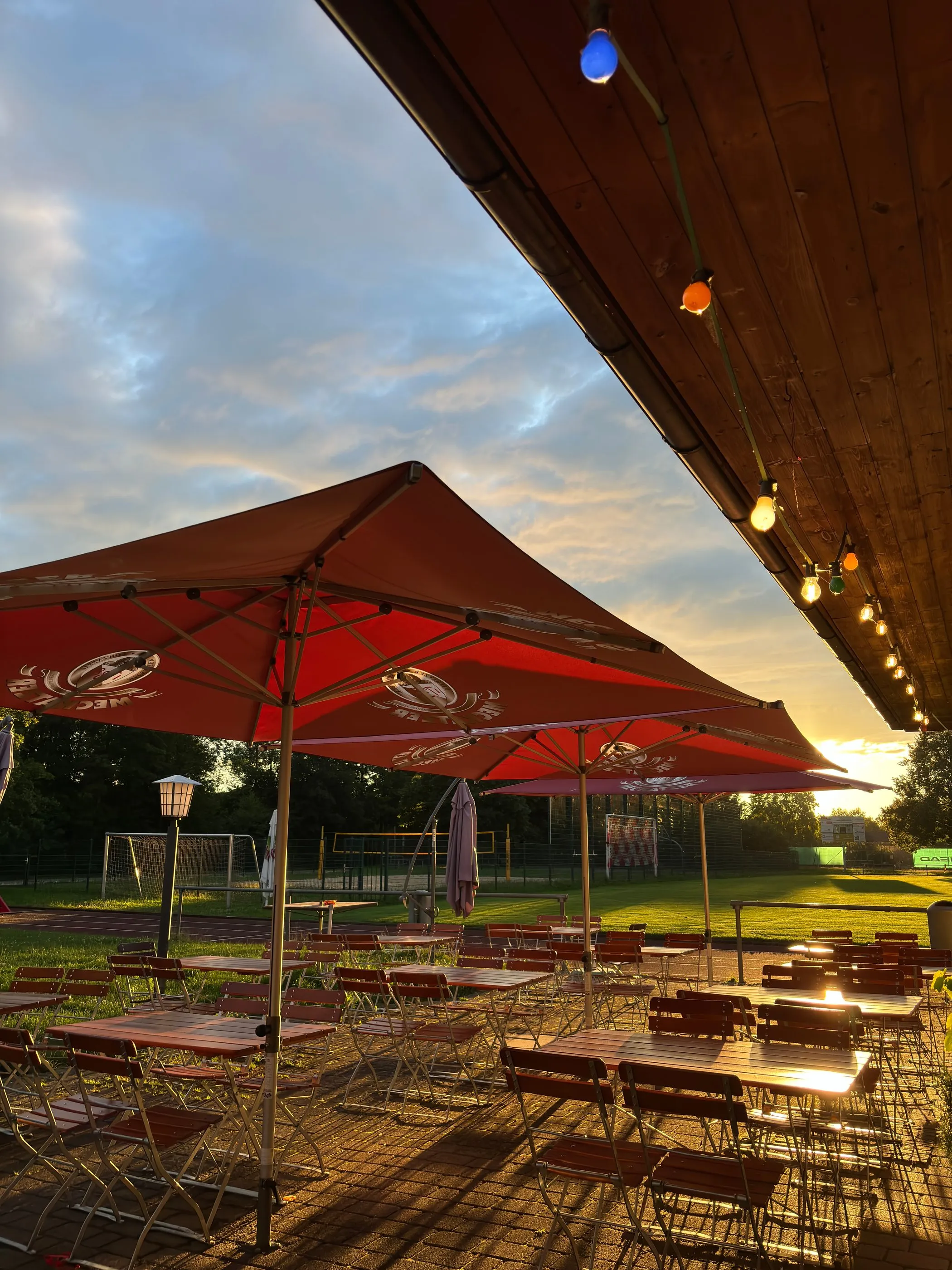 Biergarten der FC-Kluftern-Gaststätte mit roten Sonnenschirmen und Lichterketten in der Abendsonne