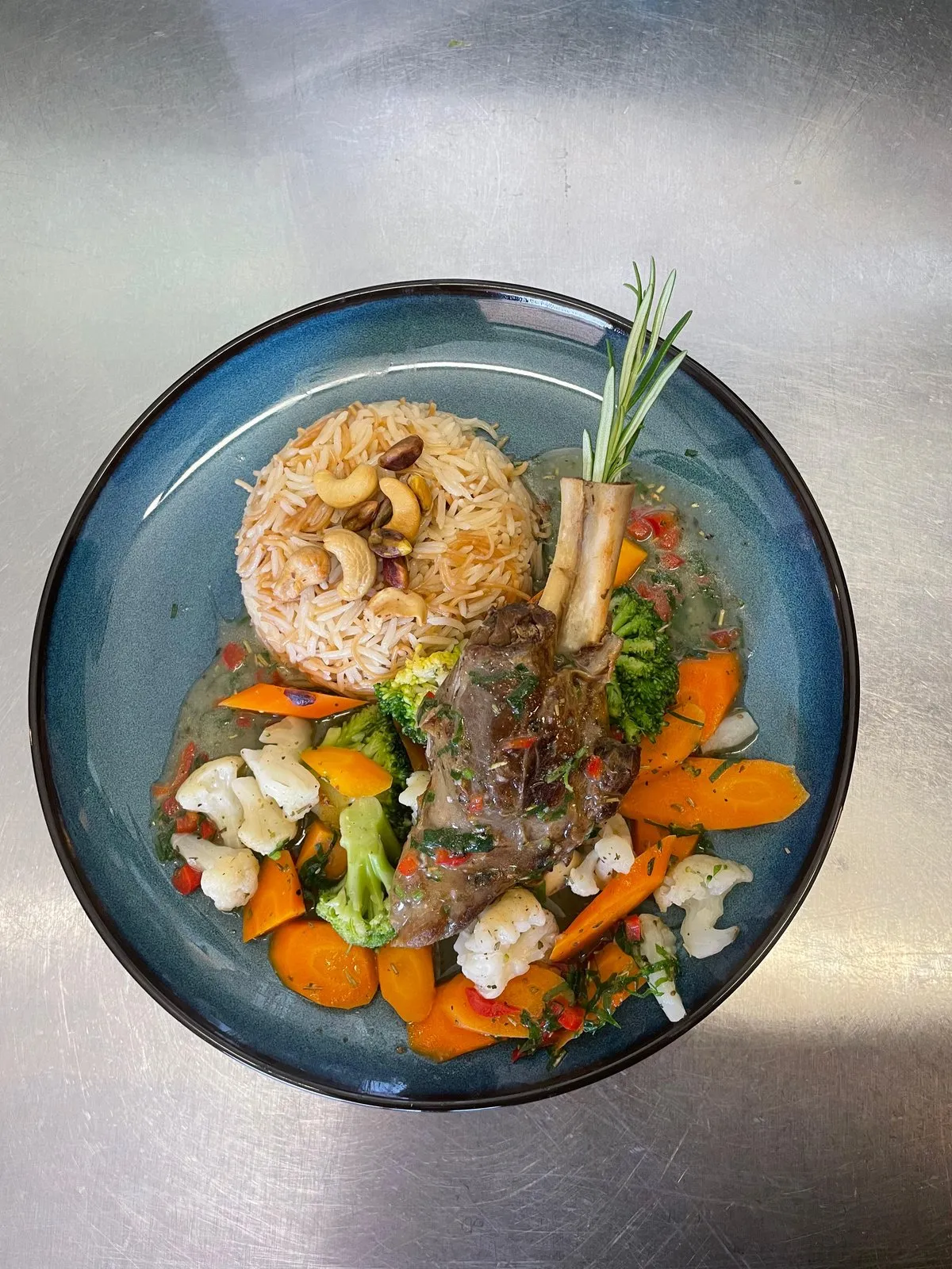 Geschmorte Lammhaxe mit Cashew-Reis und Gemüse, garniert mit Rosmarin