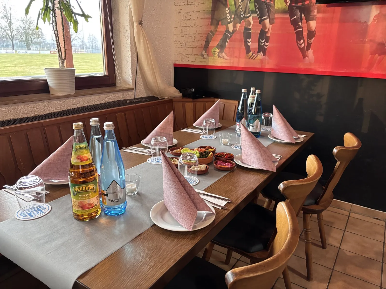 Gedeckter Tisch in der Stube mit Mazza-Schälchen, Apfelsaft und Wasser, Blick durchs Fenster auf den Sportplatz